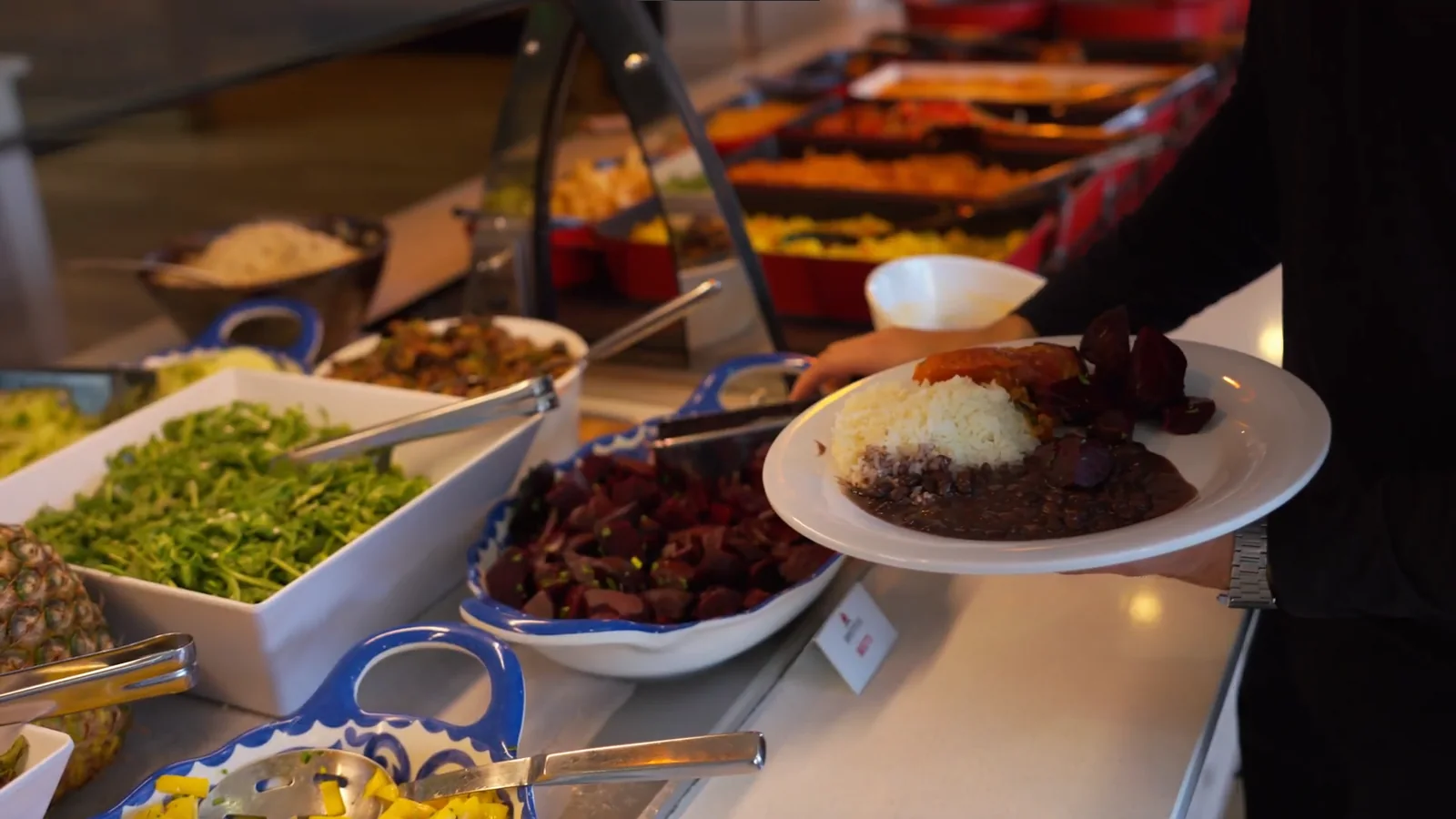 A guest holding a plate beside a colorful Brazilian buffet selection